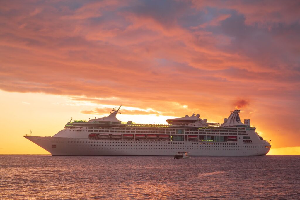 A majestic cruise ship sails across the Caribbean Sea at sunset in Grenada, showcasing a vibrant orange sky.