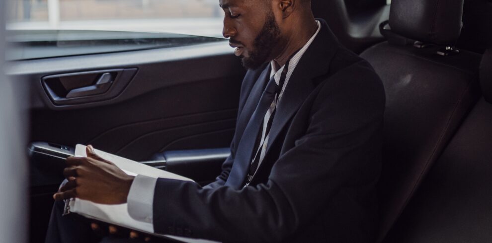 A business professional in a suit reading documents inside a car.