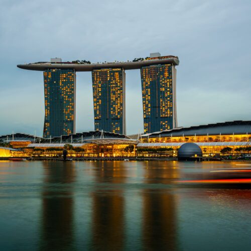 Marina Bay Sands illuminated at sunset in Singapore, reflecting on calm waters.
